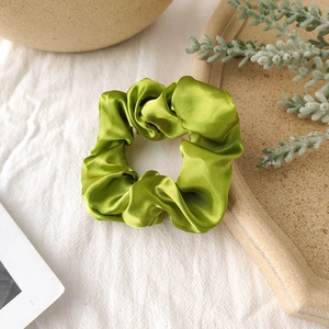 Close-up of bright green satin scrunchie with silk-like folds on a soft white background