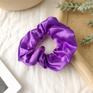 Close-up of bright purple satin scrunchie with glossy pleated texture on a tray