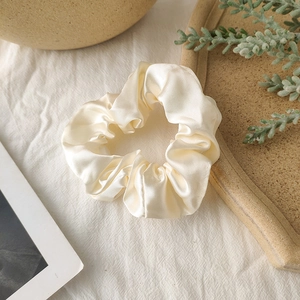 Detail of cream satin scrunchie with silky shine on white linen and ceramic plate