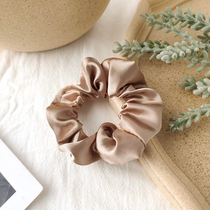 Detail of a champagne gold satin scrunchie with a glossy silk texture and elegant folds
