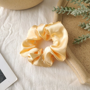 Detail of a silky pale yellow satin scrunchie resting on a textured white linen fabric