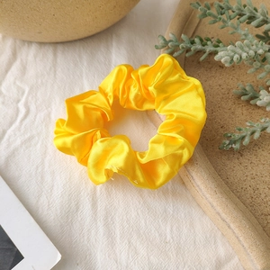 Detailed view of yellow satin silk scrunchie on a rustic wooden plate and white fabric