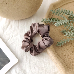 Detail of a brown satin scrunchie with silk texture on white textured fabric background
