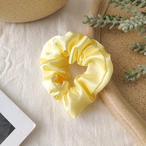 Detail of bright yellow satin scrunchie on white fabric with elegant natural accents