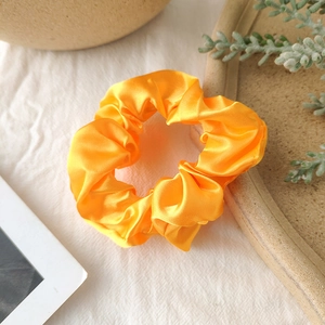 Close-up of bright orange satin scrunchie with silky texture on white fabric