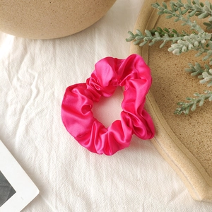 Macro view of bright magenta satin scrunchie showing glossy fabric and pleated texture