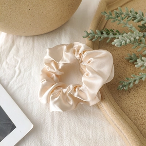 Detailed view of champagne satin scrunchie showing smooth silk texture and soft shine