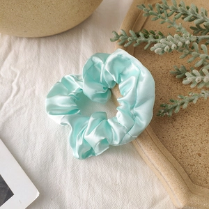 Detail of mint green satin scrunchie showing glossy fabric texture and soft pleats