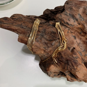 Detail of elegant gold layered chain tassel earrings resting on a rustic wood block