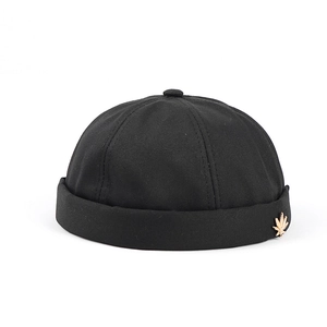Detail of black cotton docker cap featuring a gold maple leaf metal pendant on the side