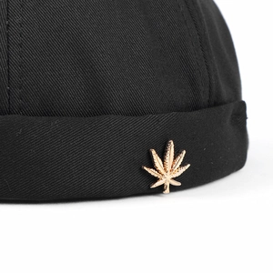 Black canvas docker hat with a golden metallic maple leaf badge on the rolled cuff