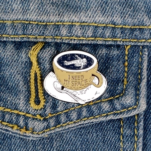 Astronaut in coffee cup enamel pin with I Need My Space text on denim jacket