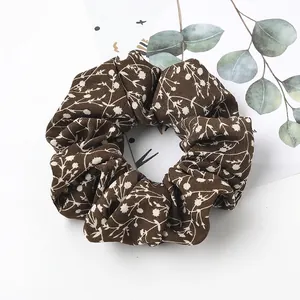 Close-up of dark brown floral scrunchie with white flower print on soft fabric texture
