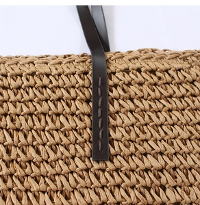 Detail of straw woven texture and dark brown leather strap with visible stitching