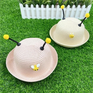 Close-up of kids straw hats with cute bee antennas and small bee figures on grass
