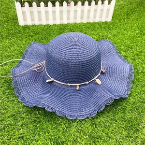 Dark blue wide brim straw hat with beaded shell detail on artificial grass