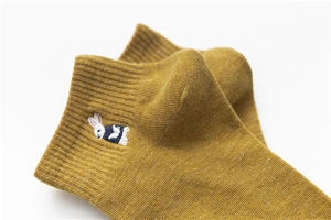 Close-up of mustard yellow cotton sock featuring cute white and blue rabbit embroidery detail