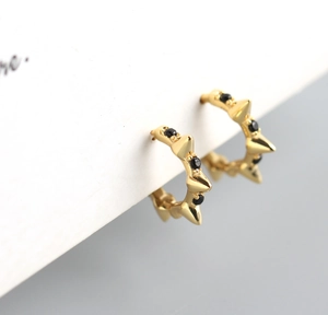 Macro shot of gold spike earrings featuring black pavé stones on a premium white surface