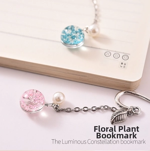 Detailed close-up of a glass flower bookmark with metal leaf pendant on a notebook