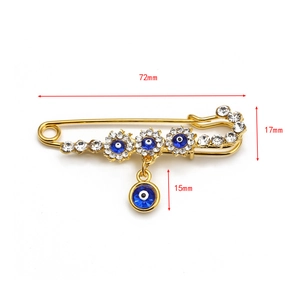 Macro view of gold safety pin brooch with blue evil eye charm and crystal accents