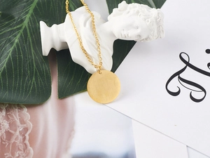 Detail of 18K gold-plated Elizabeth coin necklace displayed on a minimalist white sculpture