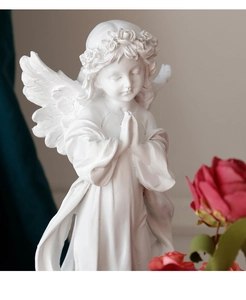 Close-up of a white praying angel sculpture showing fine wing textures and floral wreath