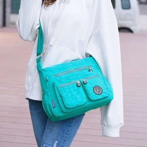 Detail of teal nylon multi-pocket crossbody bag with adjustable strap and metal hardware