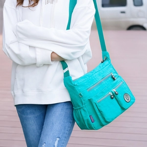 Detail of teal waterproof nylon crossbody bag featuring multiple zipper pockets on model