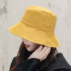 Dettaglio ravvicinato di un cappello da pescatore giallo con ricamo HAVING bianco