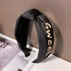 Detail of a black satin knotted headband featuring gold Sweet embroidered lettering
