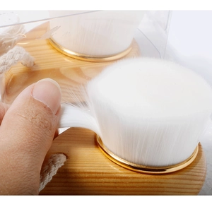 Close-up of hand holding facial brush showing soft white bristles and natural beech wood handle