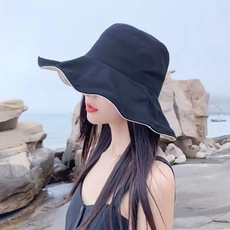 Dettaglio cappello da sole nero a tesa larga con bordi ondulati da donna al mare