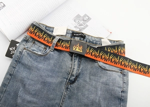 Detailed close-up of a black canvas belt featuring vibrant flame patterns on denim pants