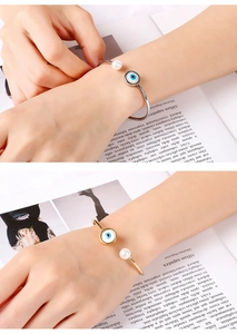 Detailed view of adjustable evil eye and pearl open bangle in gold and silver finish