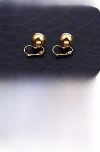 Detail view of gold ball lever-back earrings on a textured black surface