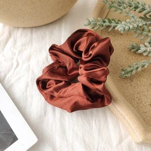Close-up of a large satin scrunchie in brick red on a white linen background