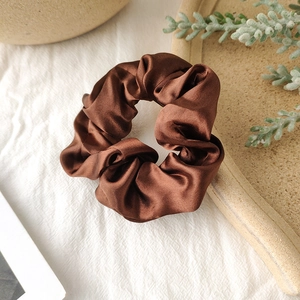 Detailed view of a brown satin scrunchie on a beige ceramic plate with soft natural lighting