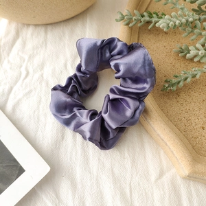 Close-up of lilac satin scrunchie on a clay tray with elegant silk texture detail