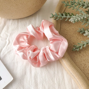 Close-up of a premium pink satin scrunchie with glossy fabric texture on linen background