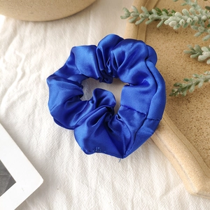 Close-up of royal blue satin scrunchie on textured linen with elegant lighting