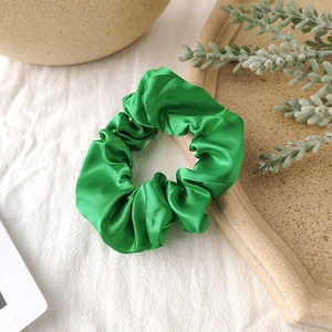 Detail of light green satin scrunchie with silky luster on a textured beige ceramic plate