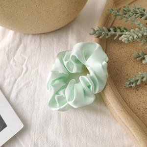 Detailed view of mint green satin scrunchie with silky folds on a textured background