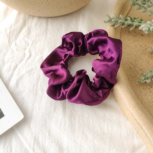 Detailed view of glossy dark purple satin scrunchie on a decorative tabletop