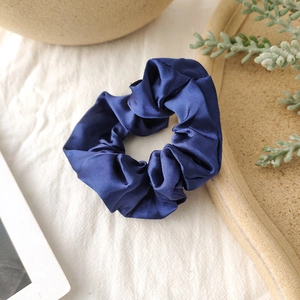 Close-up of shiny navy blue satin scrunchie on natural textured linen background