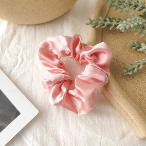 Close-up of pink satin scrunchie showing glossy fabric texture on linen background