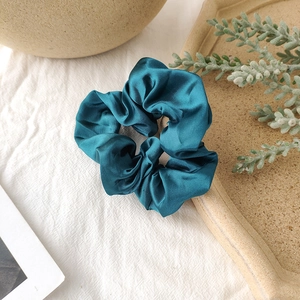 Detailed close-up of a lake blue satin scrunchie with soft pleats on a white linen cloth