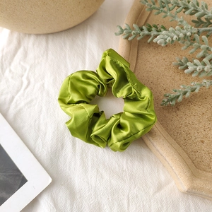 Detail shot of a soft grass green satin scrunchie resting on a rustic ceramic tray