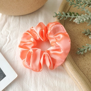 Detail of coral orange satin silk scrunchie with glossy finish and pleated design