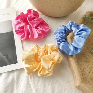Detailed close-up of glossy satin scrunchies in pink, blue, and yellow silk fabric