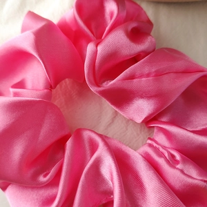 Macro shot showing texture of a glossy hot pink satin scrunchie with fine twill weaving